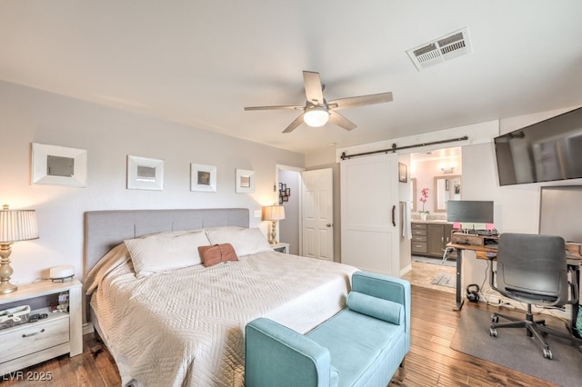 bedroom featuring connected bathroom, visible vents, a barn door, and wood finished floors