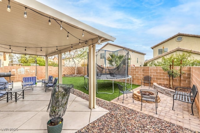 view of patio with a fire pit, a trampoline, and a fenced backyard