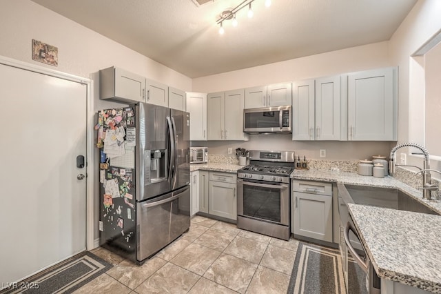 kitchen with light stone counters, visible vents, gray cabinets, a sink, and appliances with stainless steel finishes