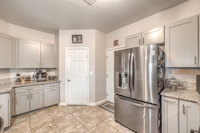 kitchen featuring light stone countertops, light tile patterned floors, gray cabinets, stainless steel fridge, and a textured ceiling