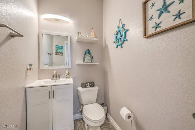 half bathroom featuring vanity, toilet, and baseboards