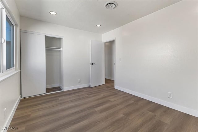 unfurnished bedroom featuring a closet, visible vents, baseboards, and wood finished floors