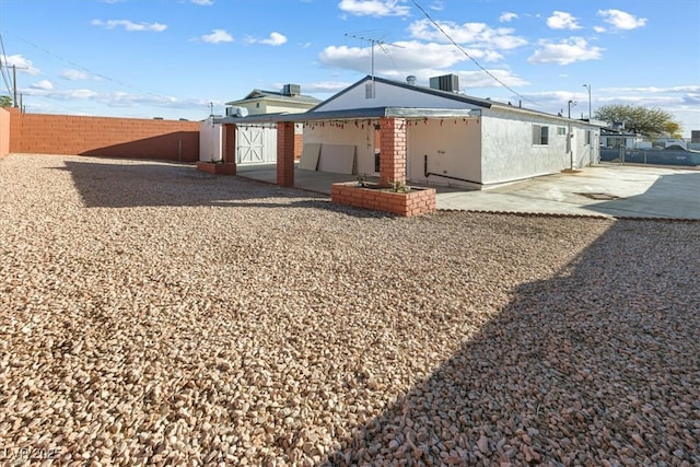 rear view of house with stucco siding, cooling unit, a fenced backyard, and a patio area