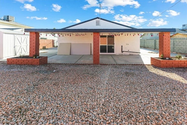 view of front facade with a patio, central AC unit, fence, and an outbuilding