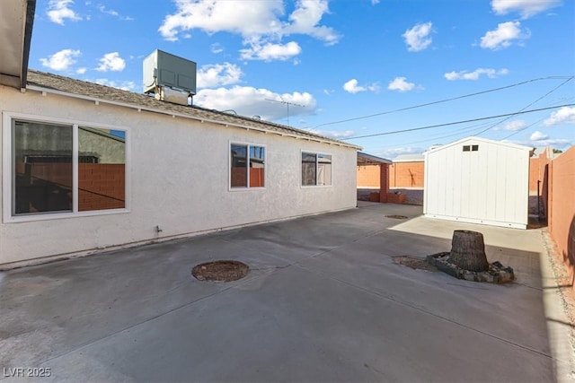 view of home's exterior featuring fence, a shed, stucco siding, an outdoor structure, and a patio