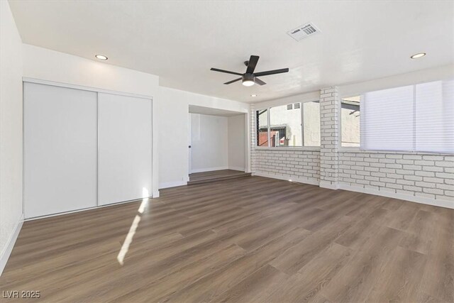 unfurnished living room featuring visible vents, wood finished floors, recessed lighting, brick wall, and ceiling fan