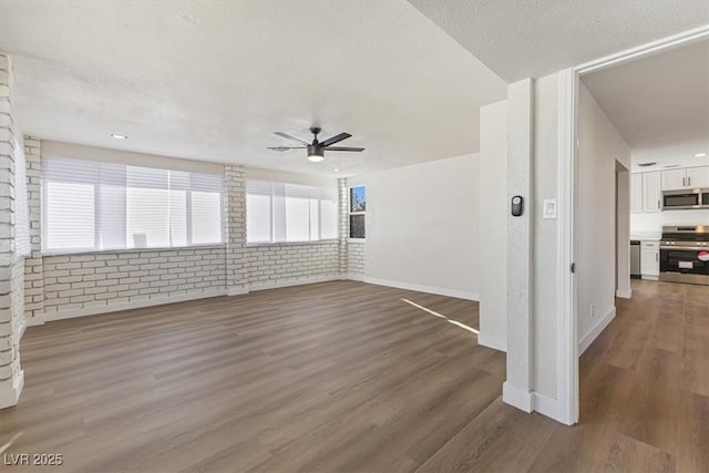 spare room with brick wall, baseboards, a ceiling fan, and wood finished floors