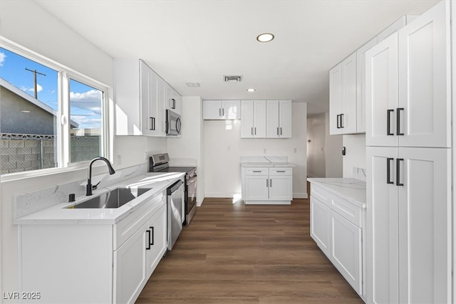 kitchen with visible vents, dark wood-type flooring, light stone countertops, appliances with stainless steel finishes, and a sink