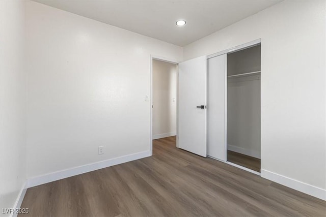 unfurnished bedroom with a closet, recessed lighting, baseboards, and wood finished floors