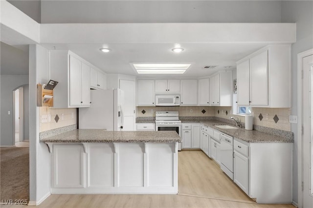 kitchen featuring a sink, white appliances, arched walkways, a peninsula, and decorative backsplash