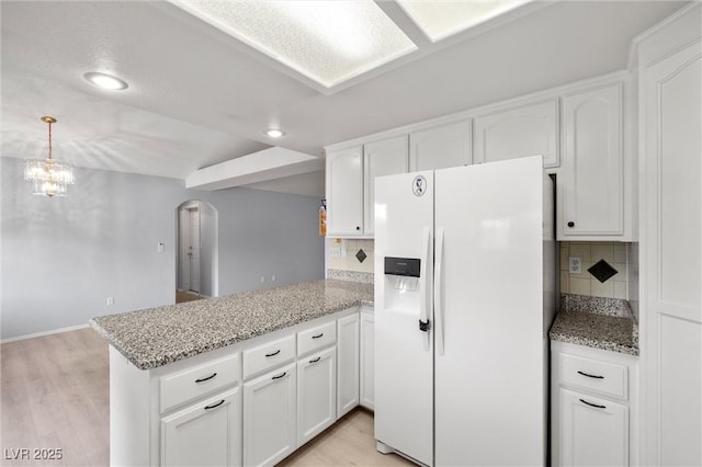 kitchen featuring light wood-type flooring, a peninsula, white refrigerator with ice dispenser, arched walkways, and white cabinetry