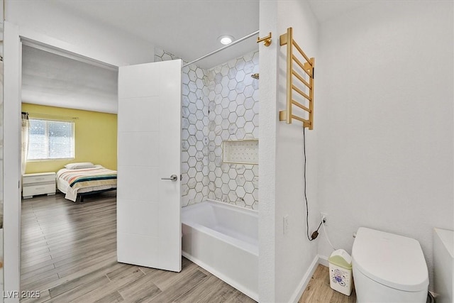 ensuite bathroom with wood finished floors, toilet, baseboards,  shower combination, and a towel warming rack