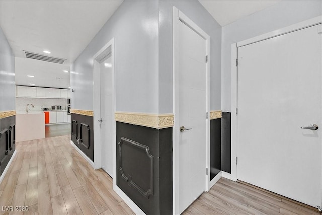 corridor featuring light wood-type flooring, recessed lighting, and a sink