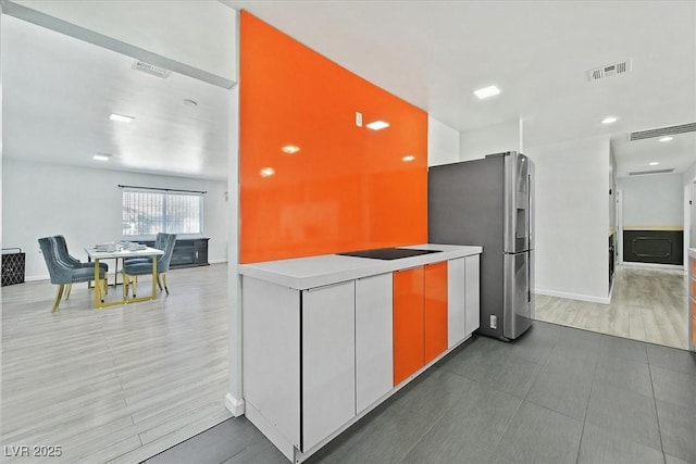 kitchen featuring stainless steel fridge with ice dispenser, light countertops, baseboards, and black electric cooktop
