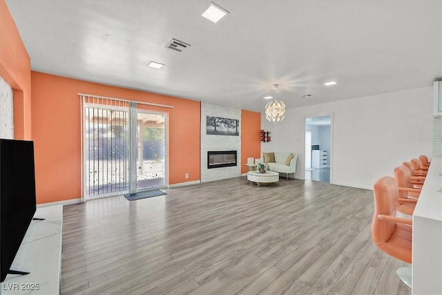 living area with light wood-type flooring, a fireplace, baseboards, and a chandelier