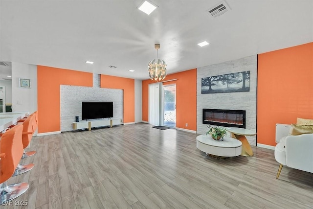 living room featuring a large fireplace, wood finished floors, a chandelier, and baseboards