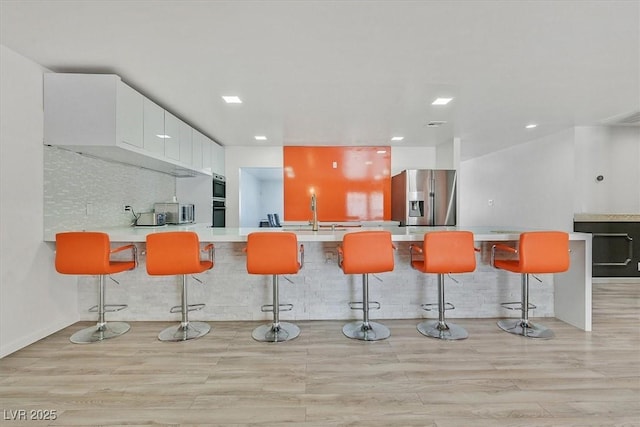 kitchen with stainless steel fridge with ice dispenser, a peninsula, light countertops, light wood-style floors, and recessed lighting