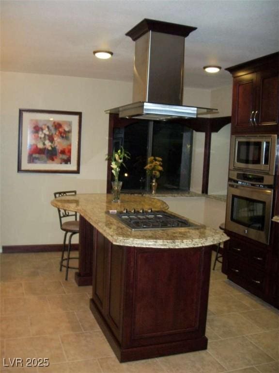 kitchen with appliances with stainless steel finishes, island range hood, baseboards, dark brown cabinets, and light stone countertops