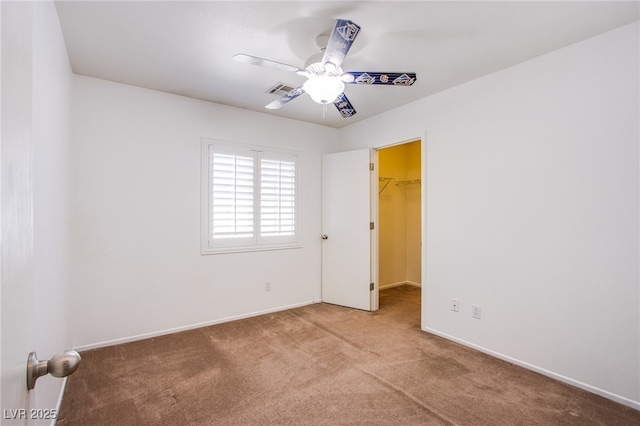 unfurnished bedroom featuring a spacious closet, ceiling fan, baseboards, and carpet floors