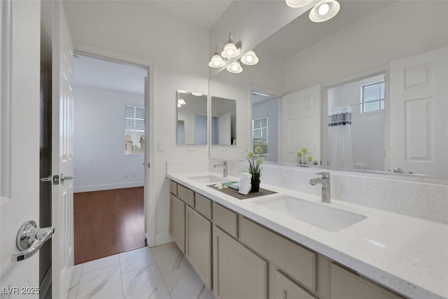 bathroom with double vanity, marble finish floor, baseboards, and a sink