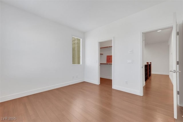 unfurnished bedroom with a walk in closet, baseboards, light wood-style floors, and a closet