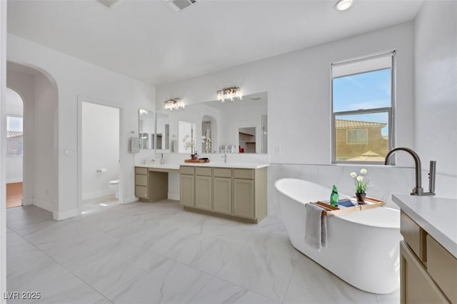 full bathroom with visible vents, toilet, a soaking tub, marble finish floor, and vanity