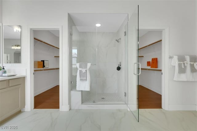 bathroom with marble finish floor, a stall shower, vanity, and a walk in closet