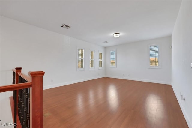 empty room with visible vents, wood finished floors, baseboards, and a healthy amount of sunlight