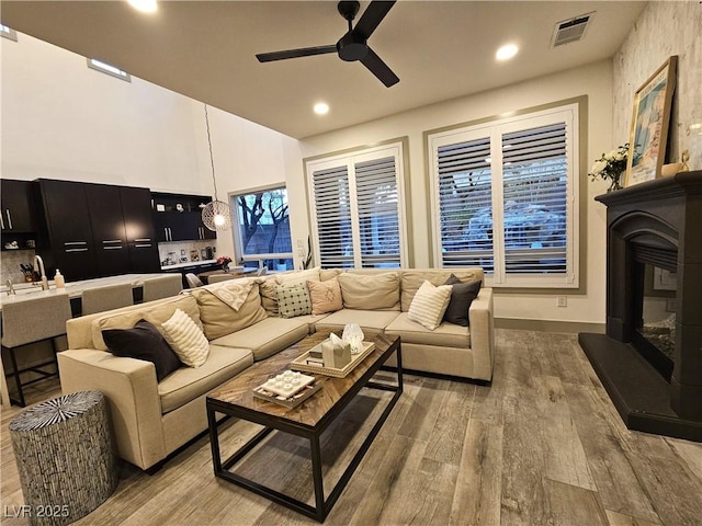 living room with wood finished floors, visible vents, a ceiling fan, recessed lighting, and a glass covered fireplace