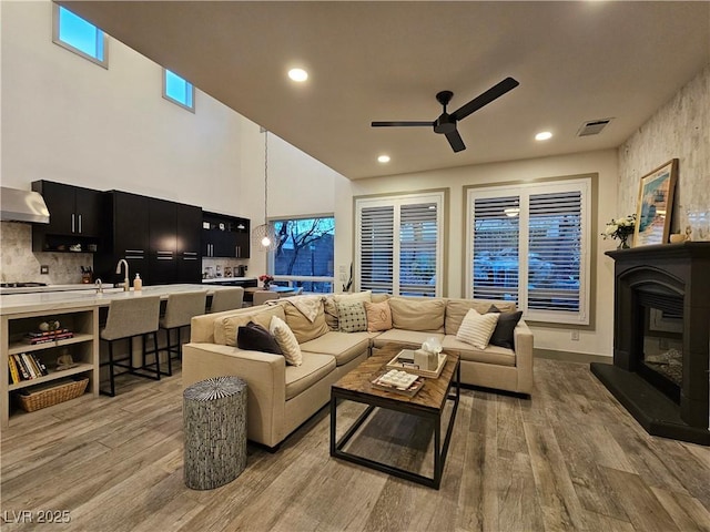 living room with light wood finished floors, visible vents, recessed lighting, a glass covered fireplace, and a ceiling fan