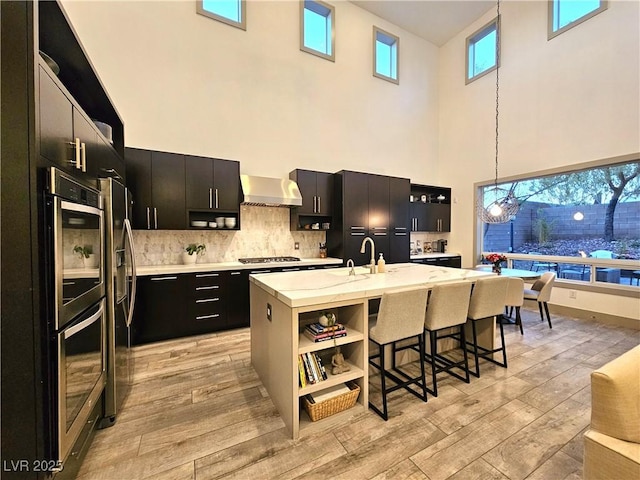 kitchen featuring a breakfast bar area, light countertops, dark cabinetry, light wood-style floors, and wall chimney exhaust hood