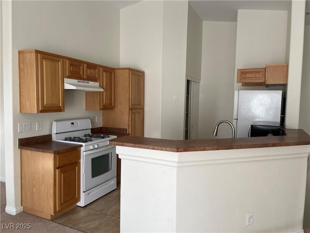 kitchen featuring white range with gas cooktop, a high ceiling, freestanding refrigerator, under cabinet range hood, and dark countertops