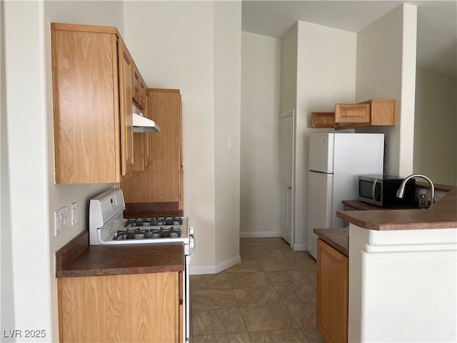 kitchen with dark countertops, stainless steel microwave, white range with gas stovetop, and under cabinet range hood