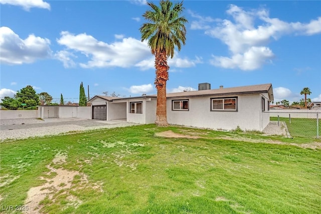 rear view of property with stucco siding, a lawn, a garage, and fence