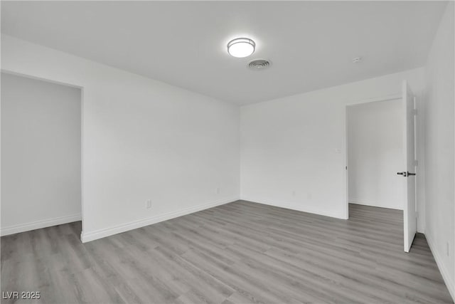 spare room with wood finished floors, visible vents, and baseboards