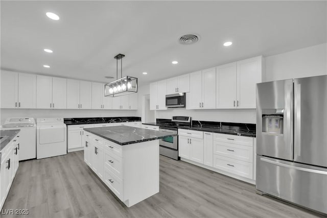 kitchen featuring light wood-type flooring, washing machine and dryer, a center island, white cabinetry, and stainless steel appliances