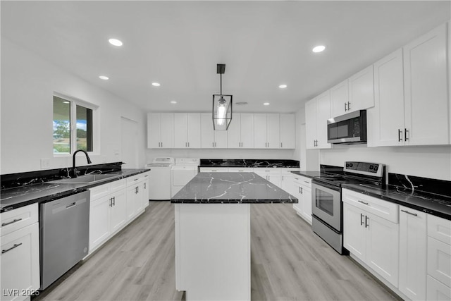 kitchen with light wood finished floors, dark stone counters, a sink, stainless steel appliances, and washer and clothes dryer