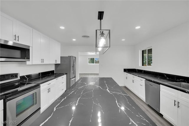 kitchen with dark stone counters, a sink, white cabinets, appliances with stainless steel finishes, and decorative light fixtures