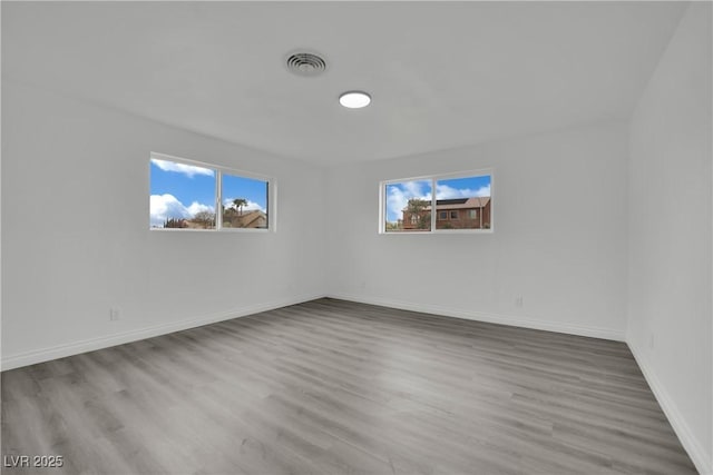 empty room with wood finished floors, visible vents, and a wealth of natural light