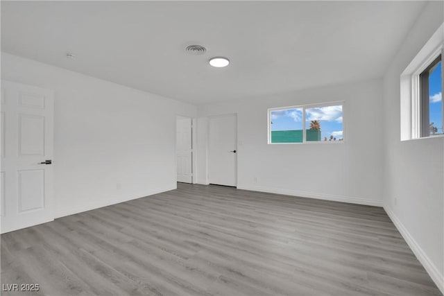 empty room with wood finished floors, a healthy amount of sunlight, and visible vents