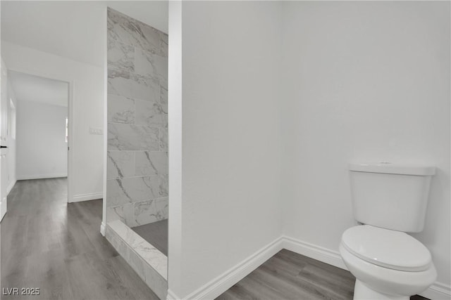 bathroom with tiled shower, toilet, baseboards, and wood finished floors