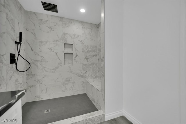 bathroom featuring visible vents, tiled shower, baseboards, and wood finished floors