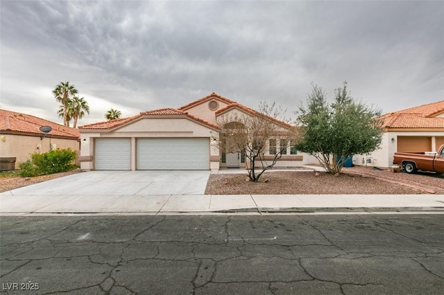 mediterranean / spanish house featuring stucco siding, concrete driveway, an attached garage, and a tile roof