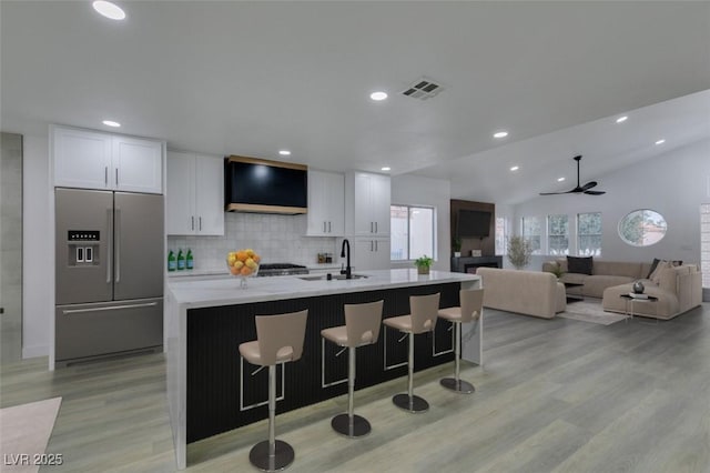 kitchen featuring range hood, visible vents, a sink, white cabinets, and stainless steel fridge