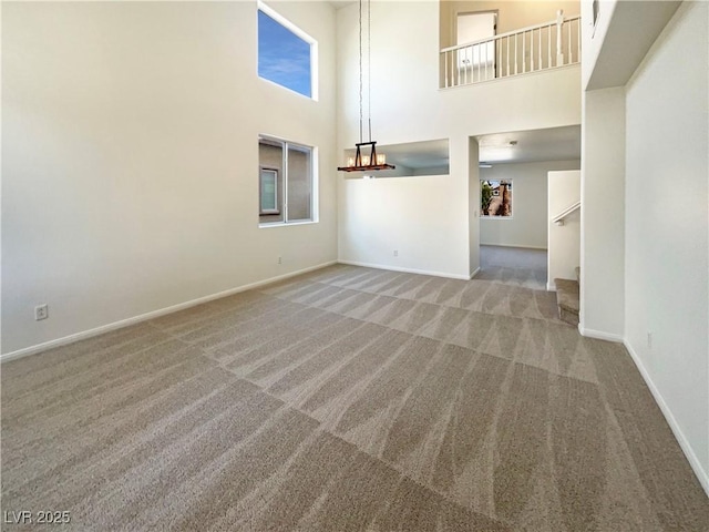 unfurnished living room featuring baseboards, carpet, stairway, a high ceiling, and an inviting chandelier