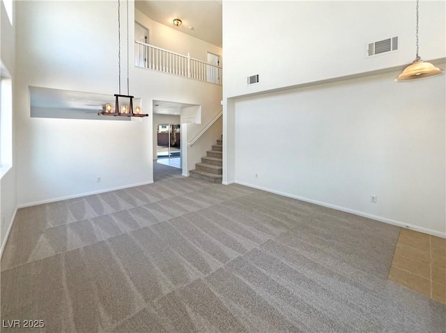 unfurnished living room featuring visible vents, baseboards, stairs, carpet floors, and a towering ceiling