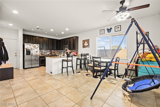 kitchen with light tile patterned floors, a peninsula, appliances with stainless steel finishes, a kitchen bar, and backsplash