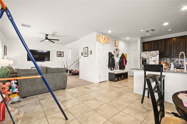 living area featuring ceiling fan, visible vents, light tile patterned flooring, and stairway