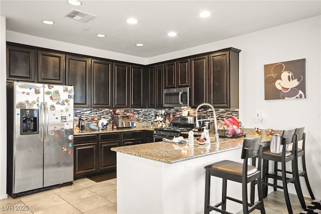 kitchen featuring tasteful backsplash, visible vents, light stone counters, a peninsula, and stainless steel appliances