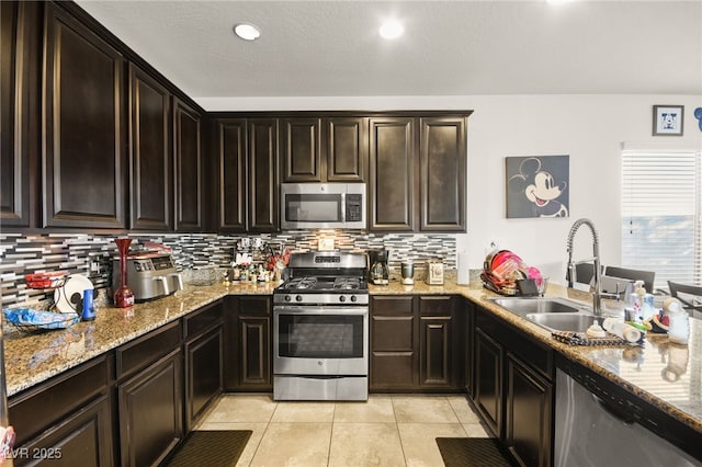 kitchen featuring tasteful backsplash, light stone countertops, light tile patterned flooring, stainless steel appliances, and a sink